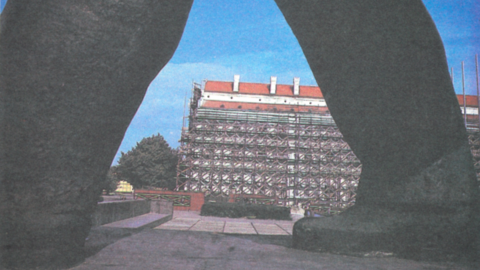 A building under construction seen in the distance through the legs of a statue