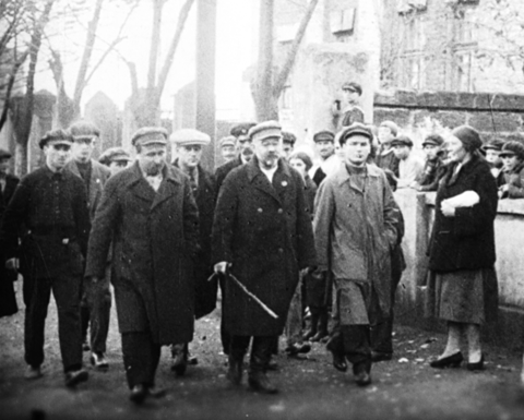 black and white photo of men walking on a street surrounded by onlookers